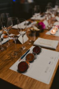 A wine tasting table set with empty glasses, tasting notes, and sample capsules in a dimly lit room