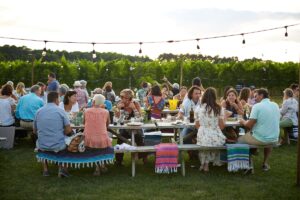 People seated at outdoor tables in a vineyard setting for a winery event