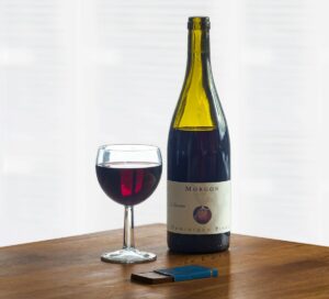 White labeled wine bottle beside glass on warm wooden table