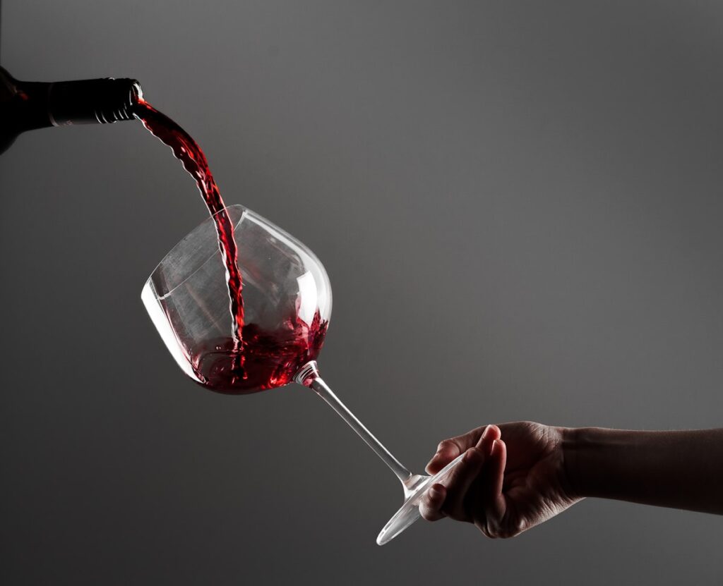 Hand holding wine glass with red wine being poured craft moment