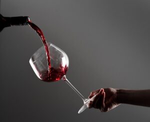 Hand holding wine glass with red wine being poured craft moment