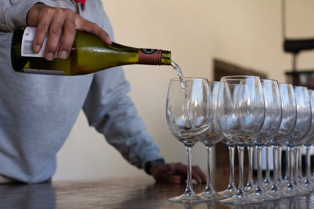 Tasting room staff member pouring wine into a row of glasses